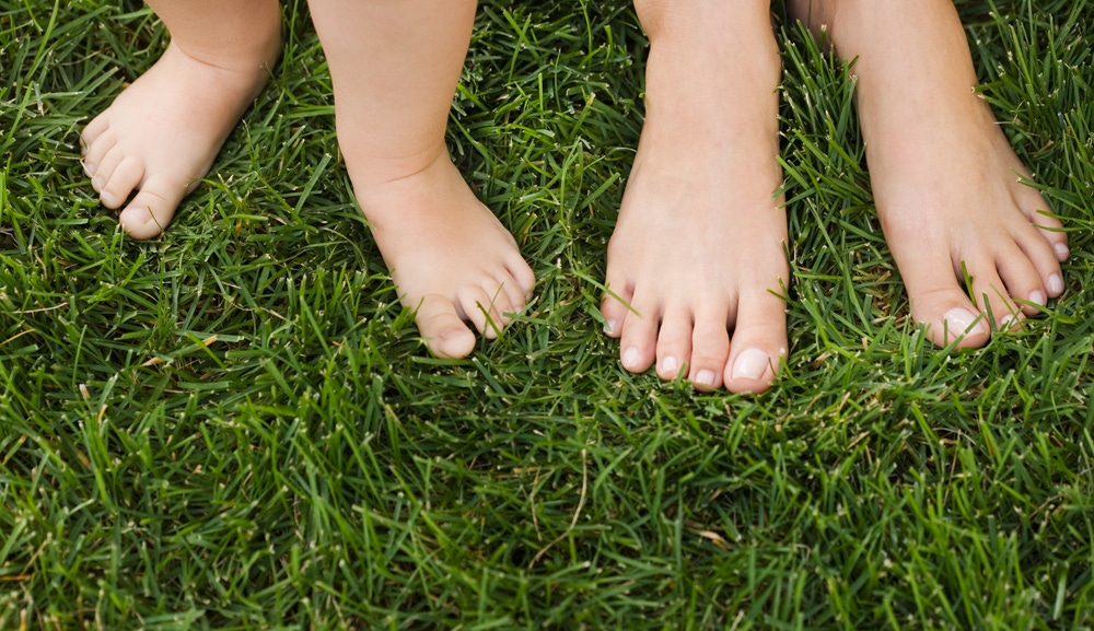 prim plan cu picioarele mamei si copilului in iarba 