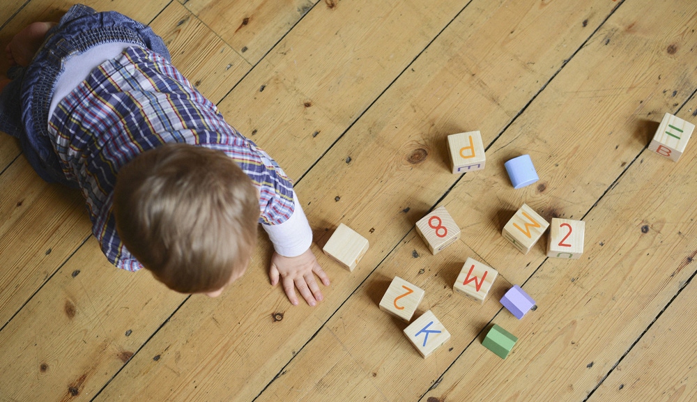 bebelus care se joaca pe podea cu cuburi de lemn