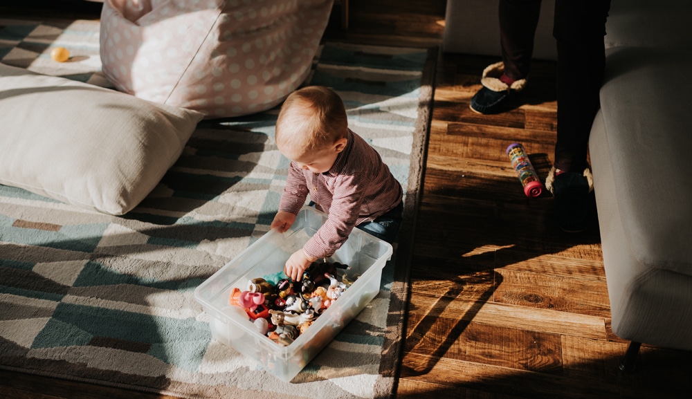 bebelus pe podea langa o cutie din plastic cu jucarii