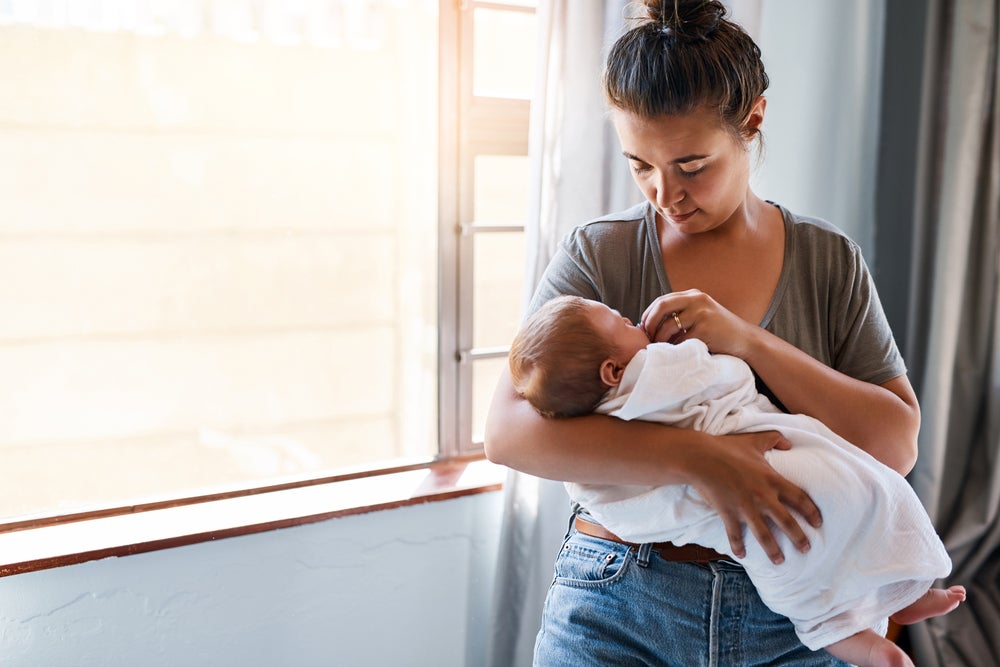 mama care tine in brate bebelusul si ii sa biberonul