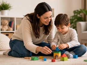 Mamă zâmbitoare ajutând copilul să deseneze la masă în living