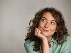 Photo of a smiling woman with curly hair resting her chin on her hand, looking up