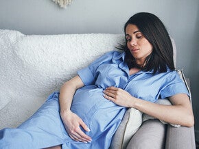 Photo of pregnant woman in blue gown reclining on couch, hand on belly.