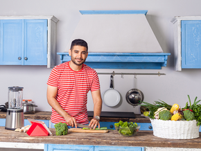 Photo of smiling man in red-striped shirt chopping vegetables in blue kitchen