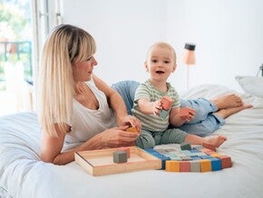 Mama si bebe stau pe pat si se joaca cu cuburi Montessori