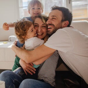 O familie vesela care râde impreuna pe o canapea, reflectând sprijinul oferit de Nestlé FamilyNes parintilor.
