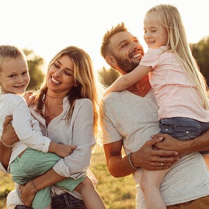 Photograph of smiling parents holding young son and daughter in sunlit grassy field