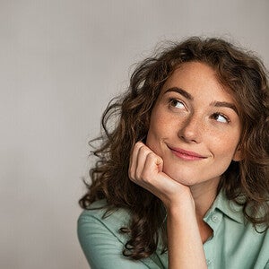 Photo of a smiling woman with curly hair resting her chin on her hand, looking up