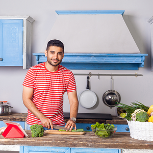 Photo of smiling man in red-striped shirt chopping vegetables in blue kitchen