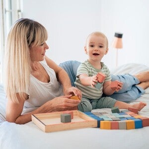 Femeie și copil pe pat, jucându-se cu cuburi colorate.