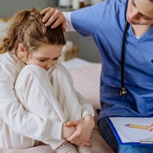 Medic îngrijorător consultă un copil pe pat, ținând un clipboard.