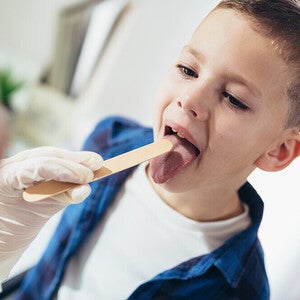 Photograph: young boy opening mouth while clinician checks throat with tongue depressor