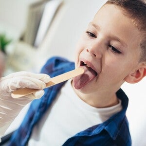 Medic examinează gâtul unui copil cu un bețișor medical.