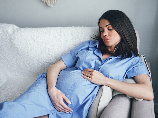 Photo of pregnant woman in blue gown reclining on couch, hand on belly.