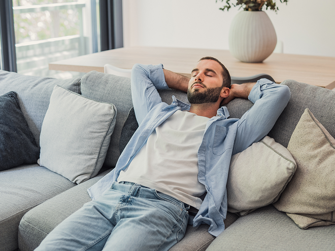 Photograph: relaxed bearded man reclining on gray sofa surrounded by cushions