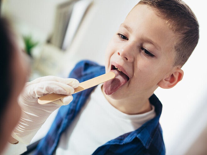 Photograph: young boy opening mouth while clinician checks throat with tongue depressor