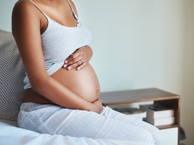 Femeie insarcinata asezata pe pat, cu mainile pe burta