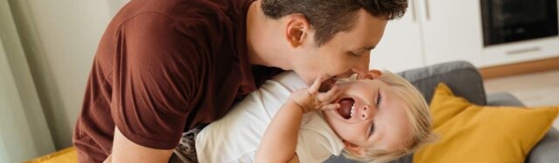 Tată jucându-se vesel cu fiul său în sufragerie.