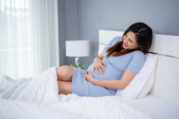 Femeie însărcinată așezată în pat, ținându-și abdomenul și resimțind disconfort abdominal în timpul sarcinii.