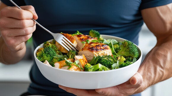 Photograph of muscular person holding a bowl of salad with grilled chicken and avocado
